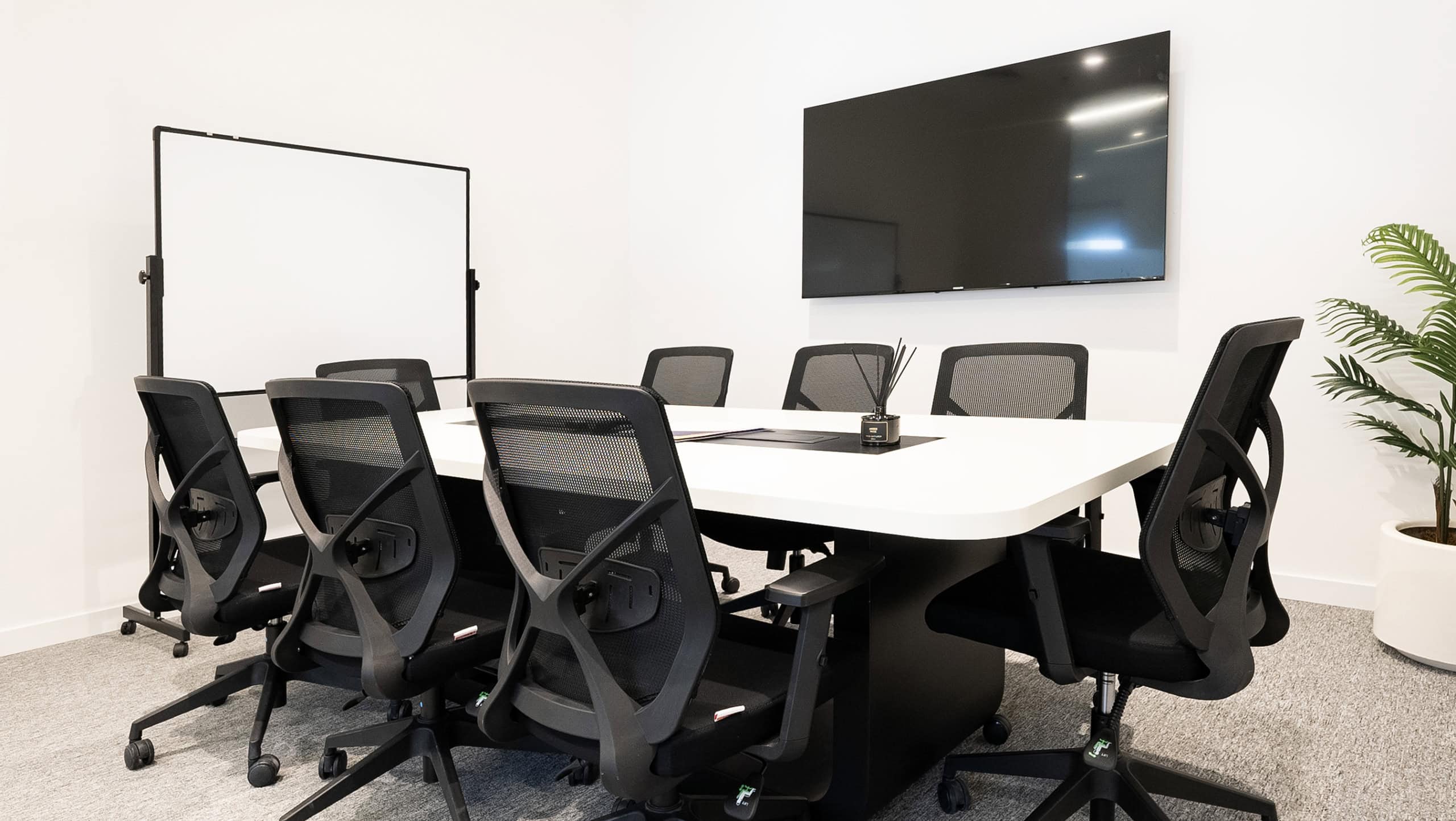 Spacious office conference room with ergonomic chairs, large screen and whiteboard for meetings and collaborative work.