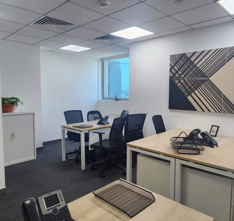 Bright UAE office with multiple workstations, black chairs, abstract artwork, and natural light.