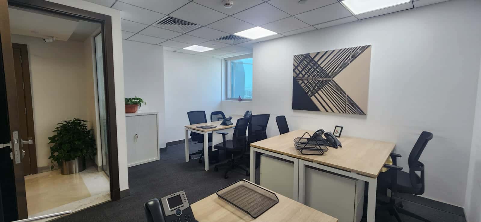Bright UAE office with multiple workstations, black chairs, abstract artwork, and natural light.