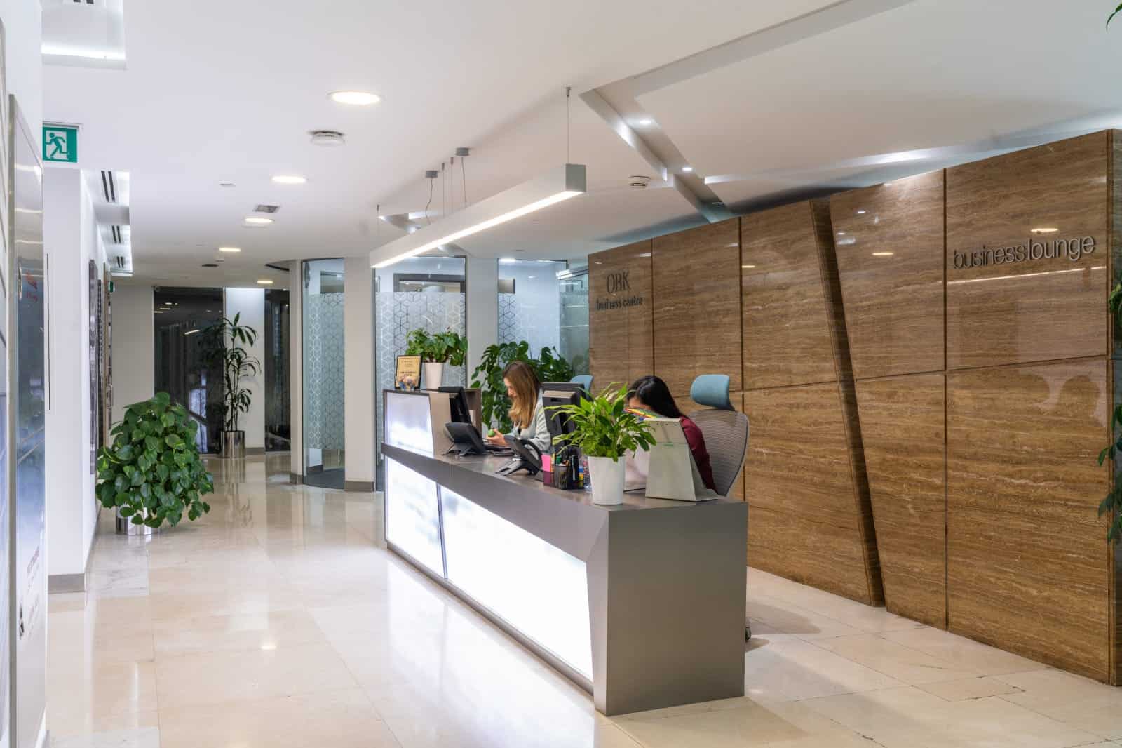 Modern reception desk with staff at work, lush green plants, welcoming office environment, business lounge in Dubai, coworking space UAE.