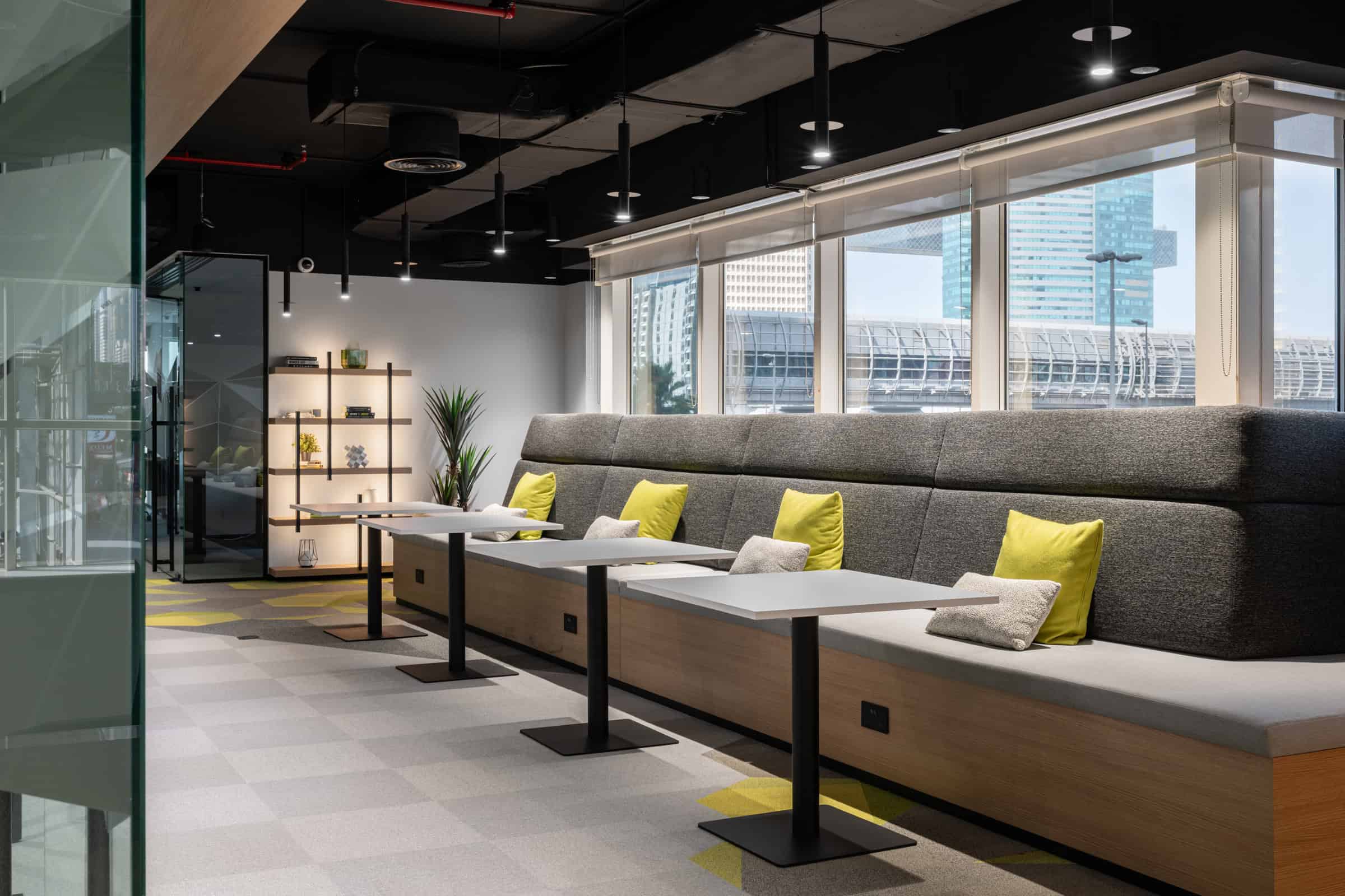 Bright coworking lounge with stylish seating, colorful cushions, and urban city views in Dubai.