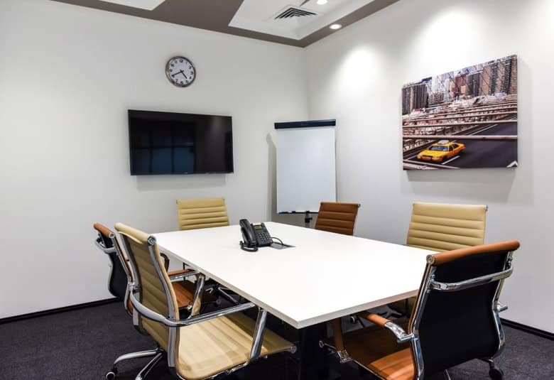 Versatile meeting room with sleek furniture, conference phone, TV, and cityscape artwork. Ideal for business meetings in UAE.