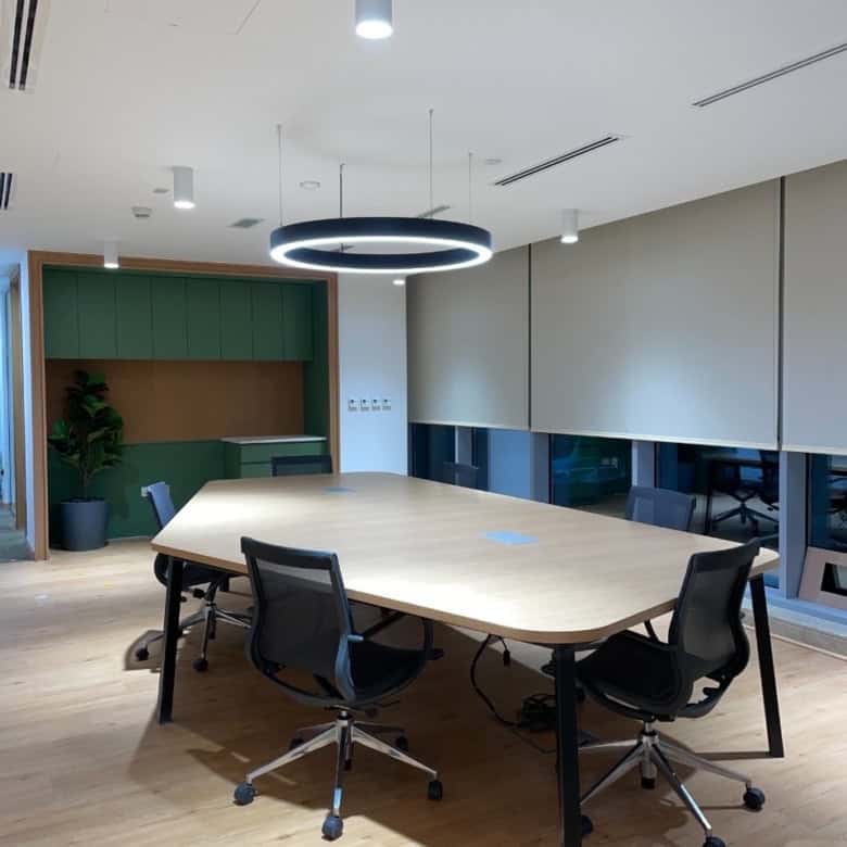 Bright, contemporary office meeting room featuring a large wooden table, black chairs, and sleek lighting for productivity.
