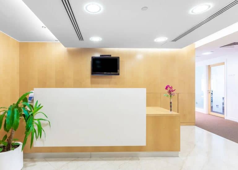 Clean, professional reception area with a wooden accent wall and digital TV display.