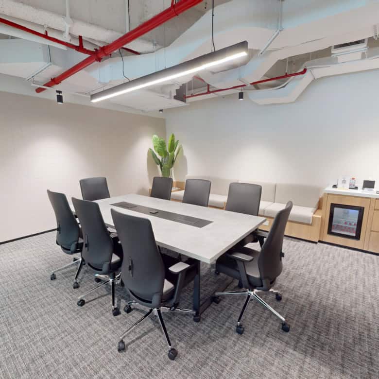 Bright, minimalist coworking meeting room featuring a large table, comfortable chairs, and tech-enabled workstations in Dubai.
