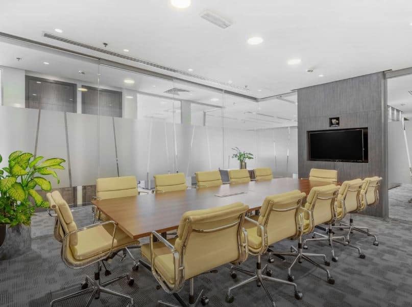 Spacious conference room with glass walls, comfortable chairs, and a large TV screen for meetings and collaborations.