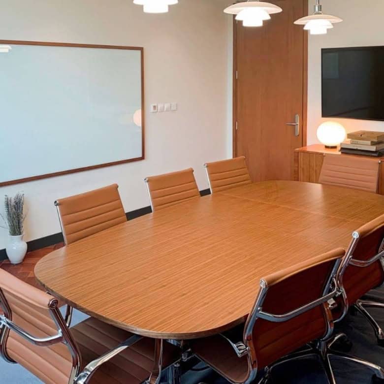 A professional conference room with a large wooden table, leather chairs, and a wall-mounted TV, perfect for meetings at Nextspace UAE.