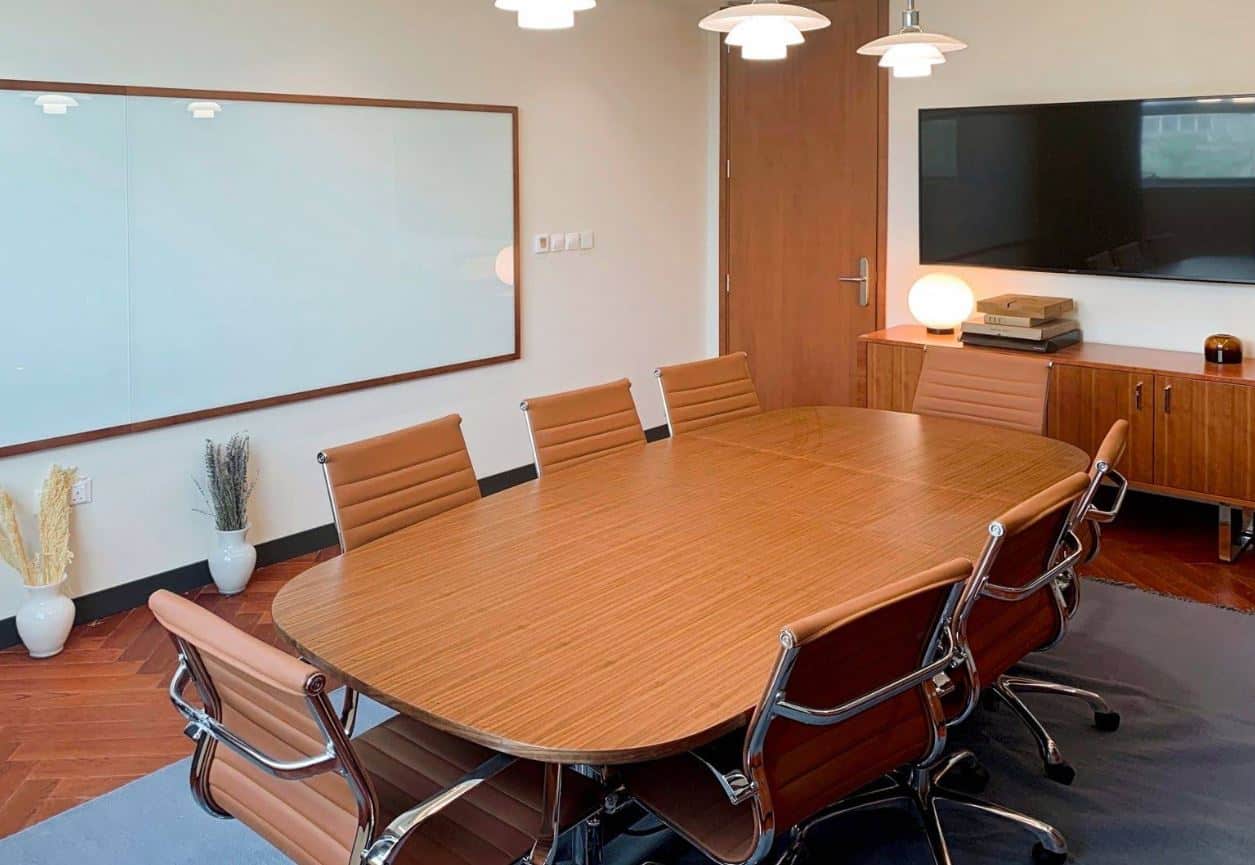 A professional conference room with a large wooden table, leather chairs, and a wall-mounted TV, perfect for meetings at Nextspace UAE.