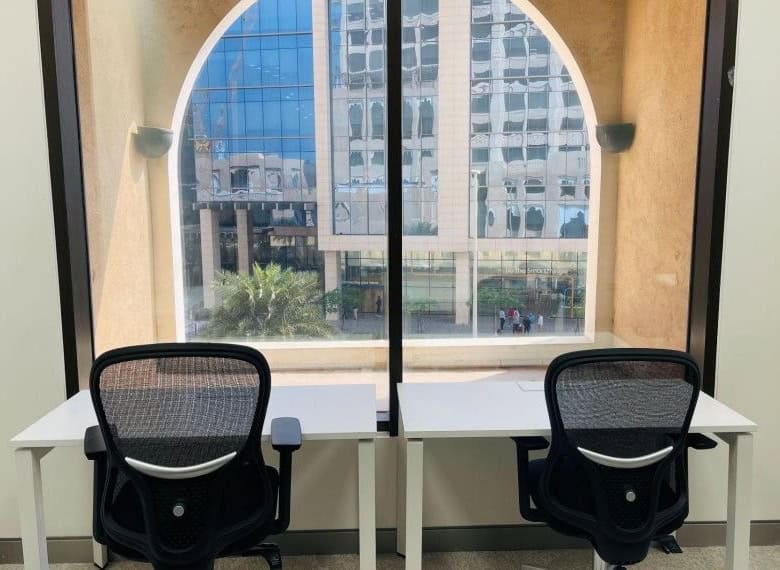 Office desks with chairs facing large window in Dubai business center.