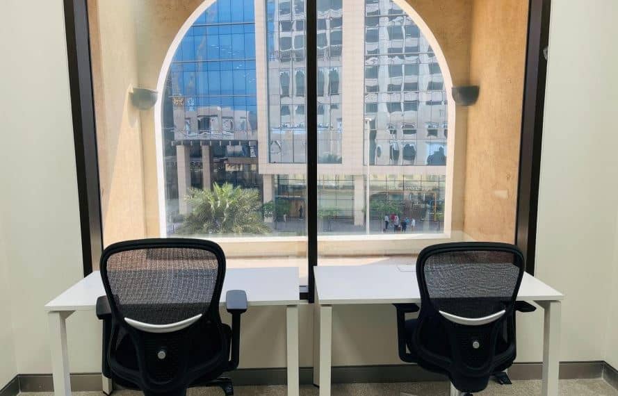 Office desks with chairs facing large window in Dubai business center.