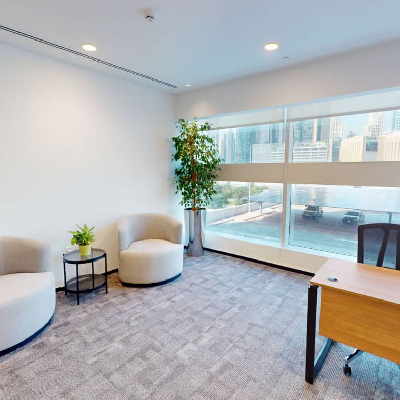 Office lounge with airy design, cozy chairs, green plants, and large windows overlooking Dubai skyline.