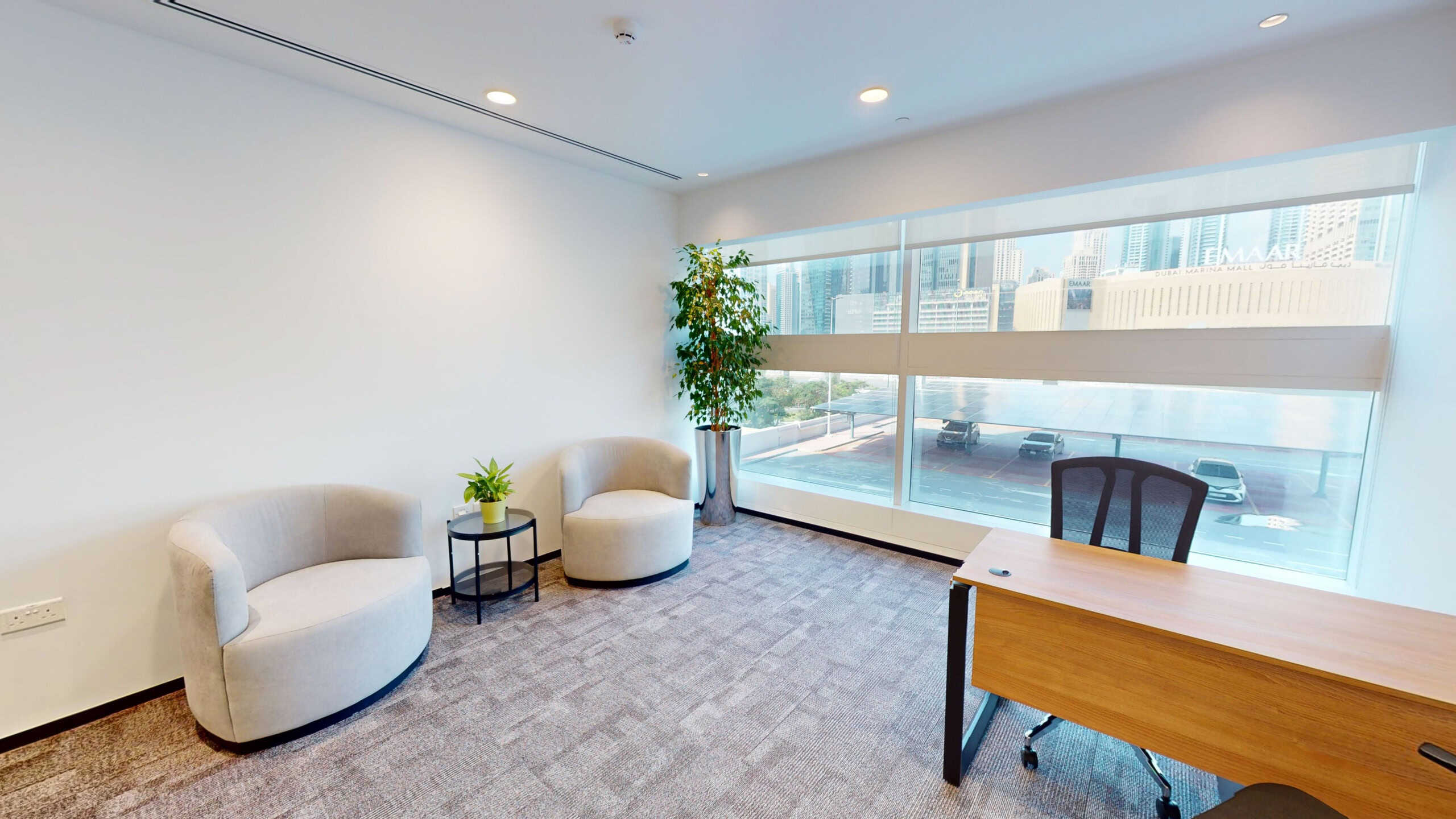 Office lounge with airy design, cozy chairs, green plants, and large windows overlooking Dubai skyline.