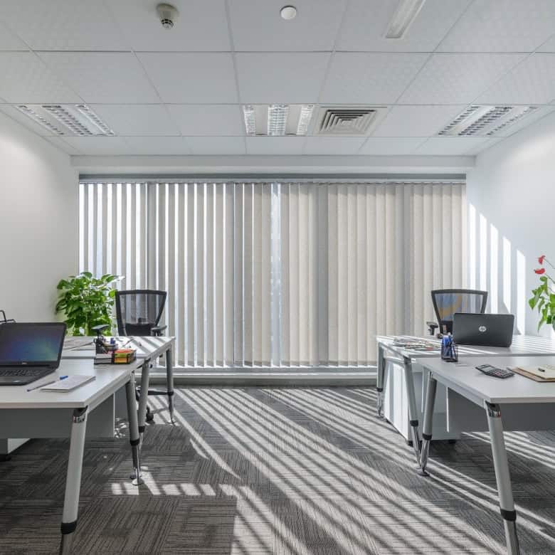 Bright modern office with desks, chairs, laptops, and large window with vertical blinds in Dubai.