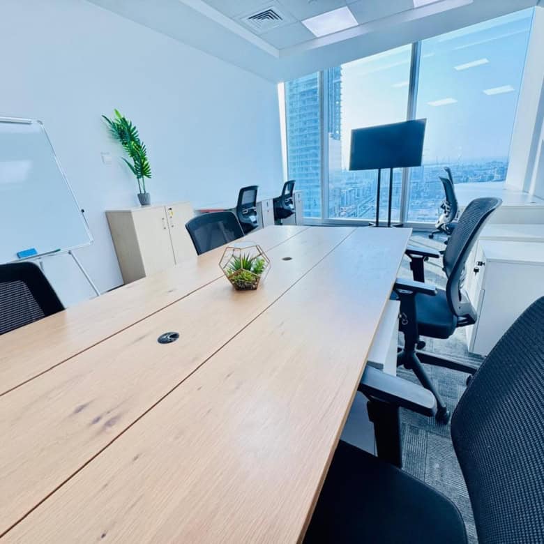 Bright office with meeting table, large screen, and city view in UAE coworking space.