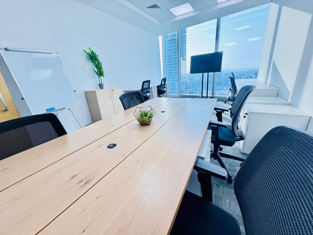 Bright office with meeting table, large screen, and city view in UAE coworking space.