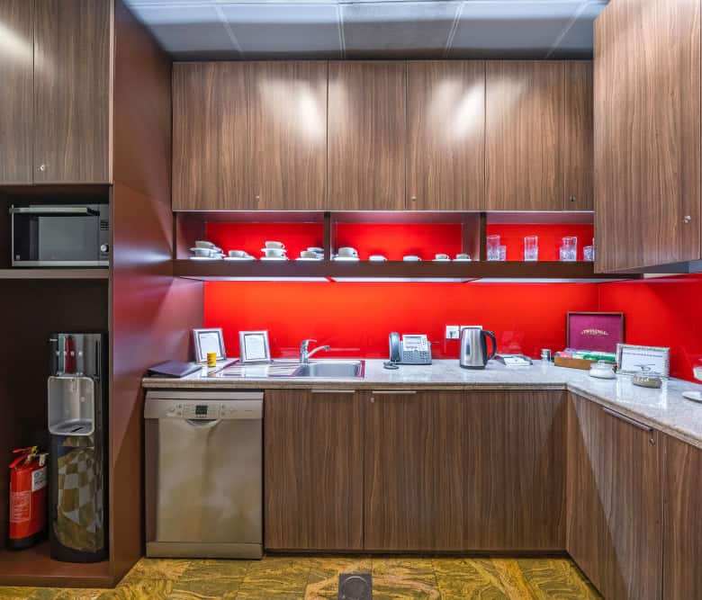 Cozy UAE coworking space kitchen featuring wooden cabinets and vibrant red backsplash.