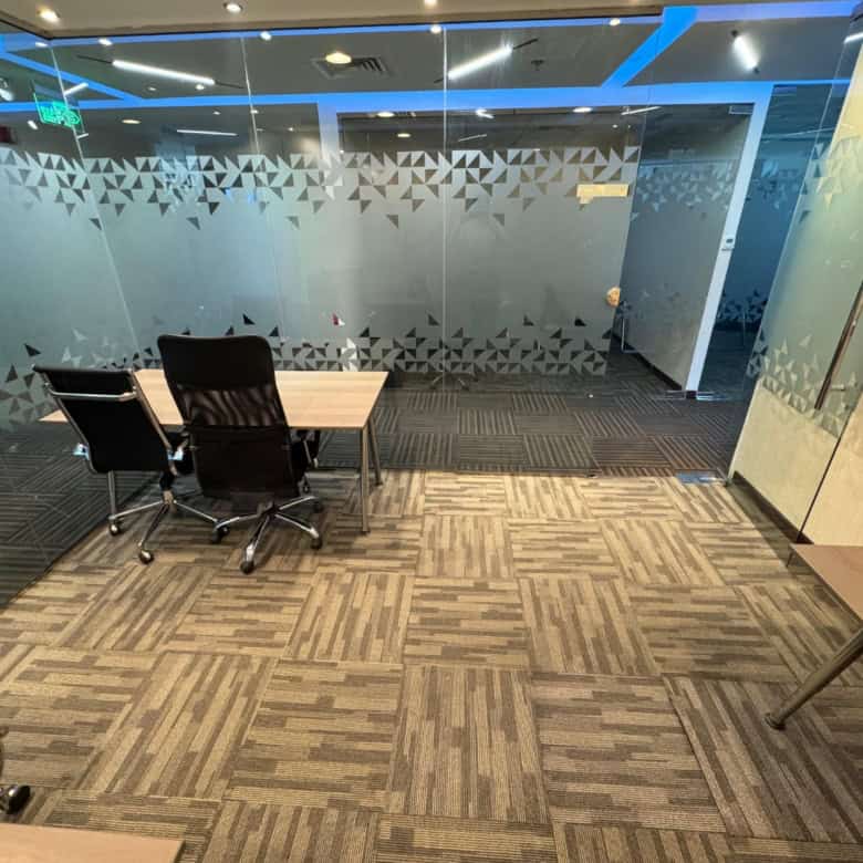 Open plan office with glass partition at Nextspace UAE featuring meeting tables, black chairs, and contemporary design aesthetics.