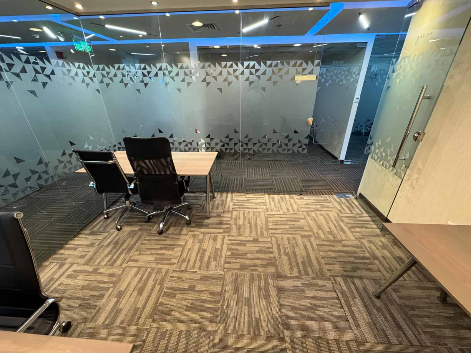 Open plan office with glass partition at Nextspace UAE featuring meeting tables, black chairs, and contemporary design aesthetics.